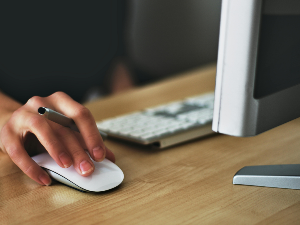 Close-up of a person using a computer mouse and keyboard in a modern office setting—symbolizing workplace stress and digital overload.